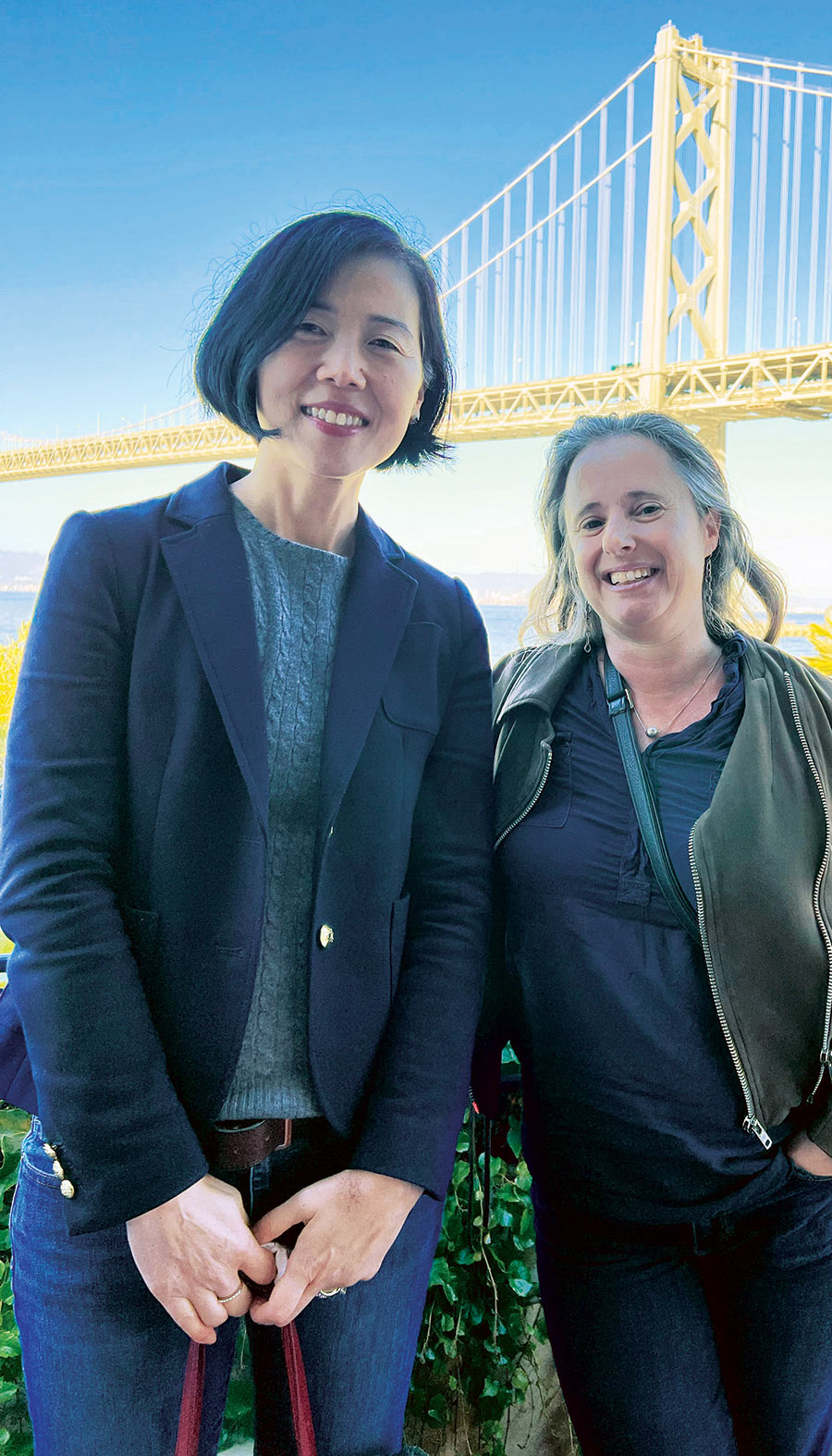 A portrait photograph of Theresa Lee and Rachel Horsch standing next to each other smiling as they pose for a picture outside