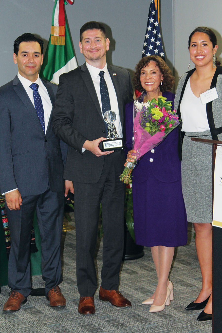 A portrait photograph of Emily Vasquez (second from right) smiling as she poses for a picture being recognized for an award