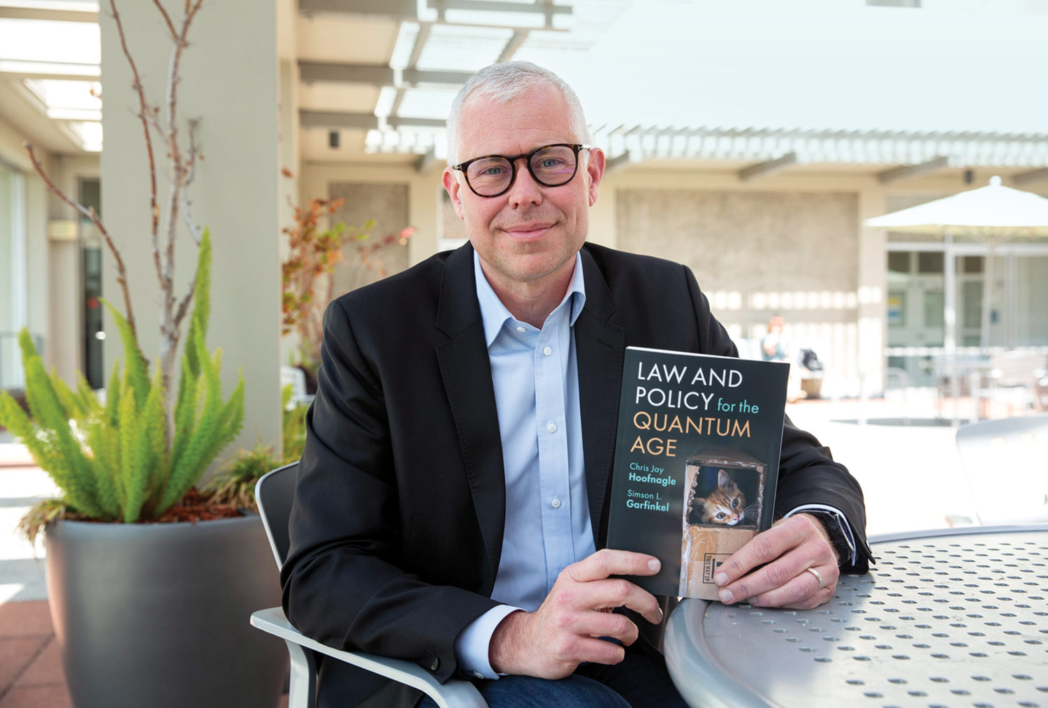 Professor Chris Hoofnagle seated at an outdoor table holding his latest book