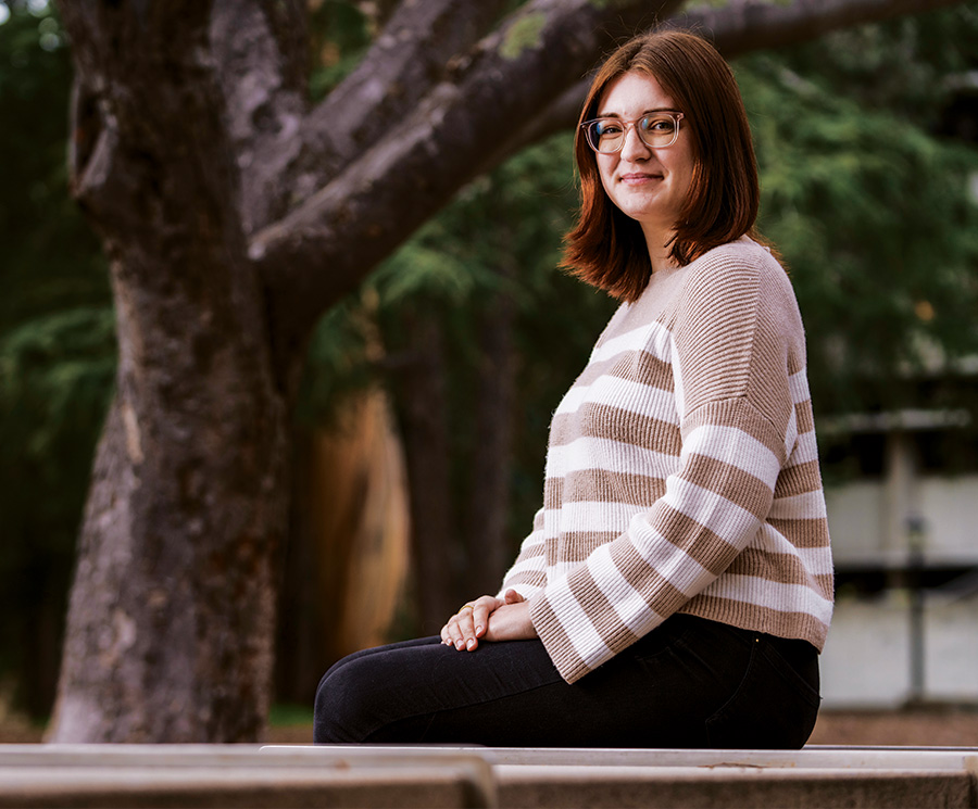 Alyssa Meurer wearing glasses and a striped beige sweater posing for a photo outdoors