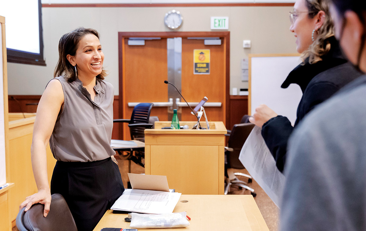 Professor Diana Reddy Ph.D. smiles while speaking to students at a desk in the front of an course room