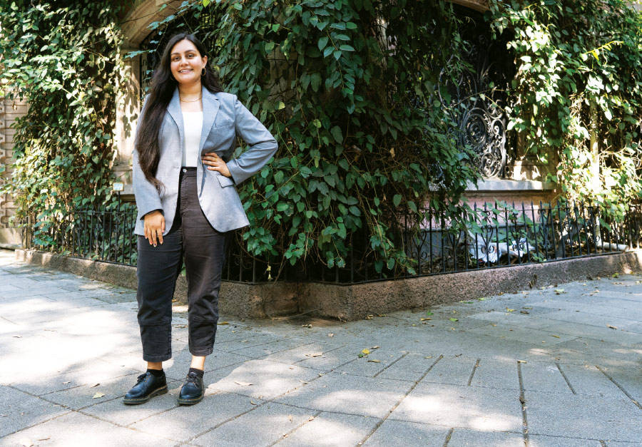 Henna Kaur Kaushal standing with hand on her hip while wearing a grey blazer and tweed pants outdoors