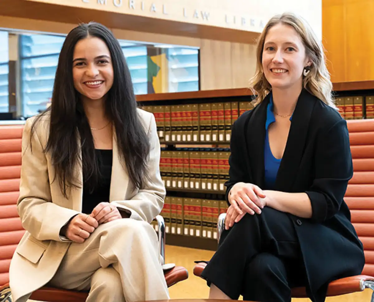 Leila Nasrolahi and Kate Walford smile and sit together inside the library