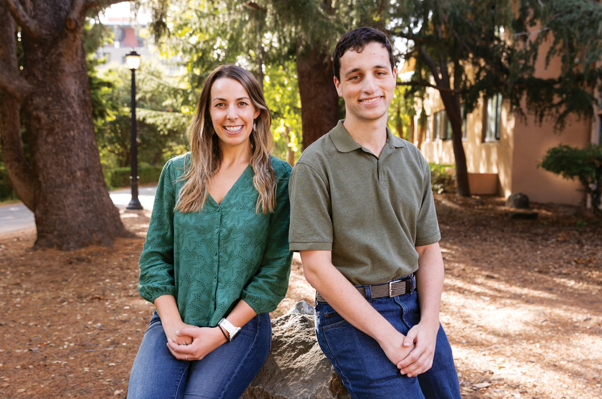 Becky Hunter wearing a green blouse and jeans sitting on a rock next to Grayson Peters wearing a olive green polo shirt and jeans 