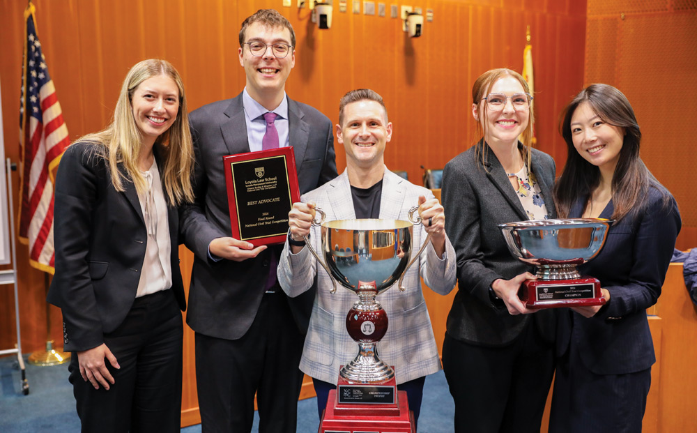 Five people holding awards and trophies, standing in a formal room.