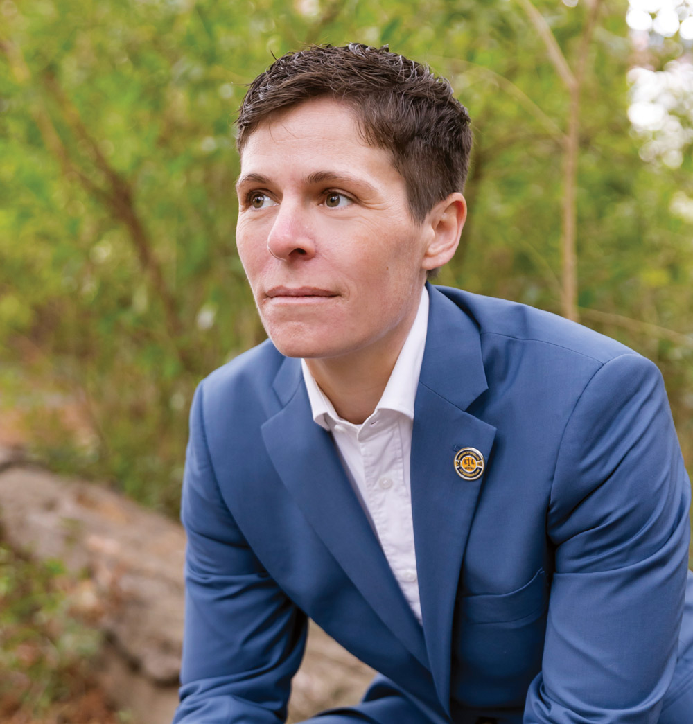 Person in a blue suit sitting on a rock with greenery in the background.