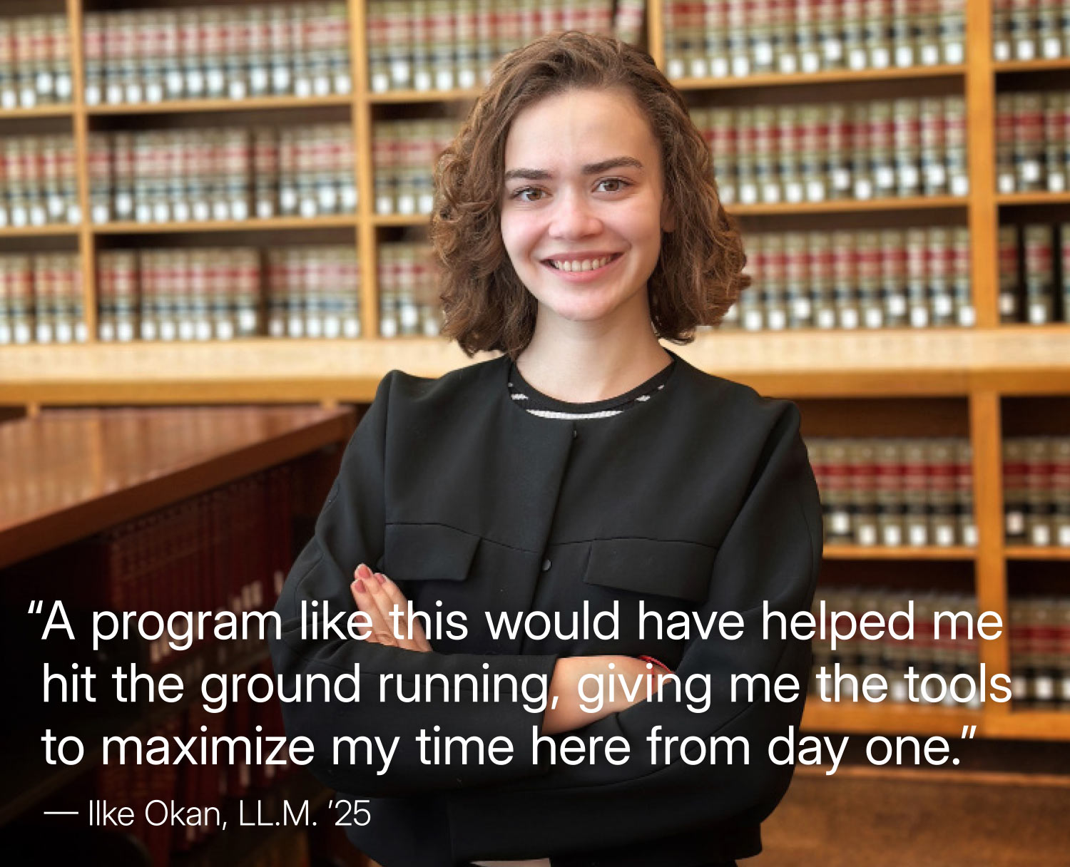 A young woman with shoulder-length brown hair and a black blazer stands in a library. She is smiling directly at the camera with her arms crossed. Behind her are rows of legal books on shelves; quote by Ilke Okan, LL.M. ’25: "A program like this would have helped me hit the ground running, giving me the tools to maximize my time here from day one."